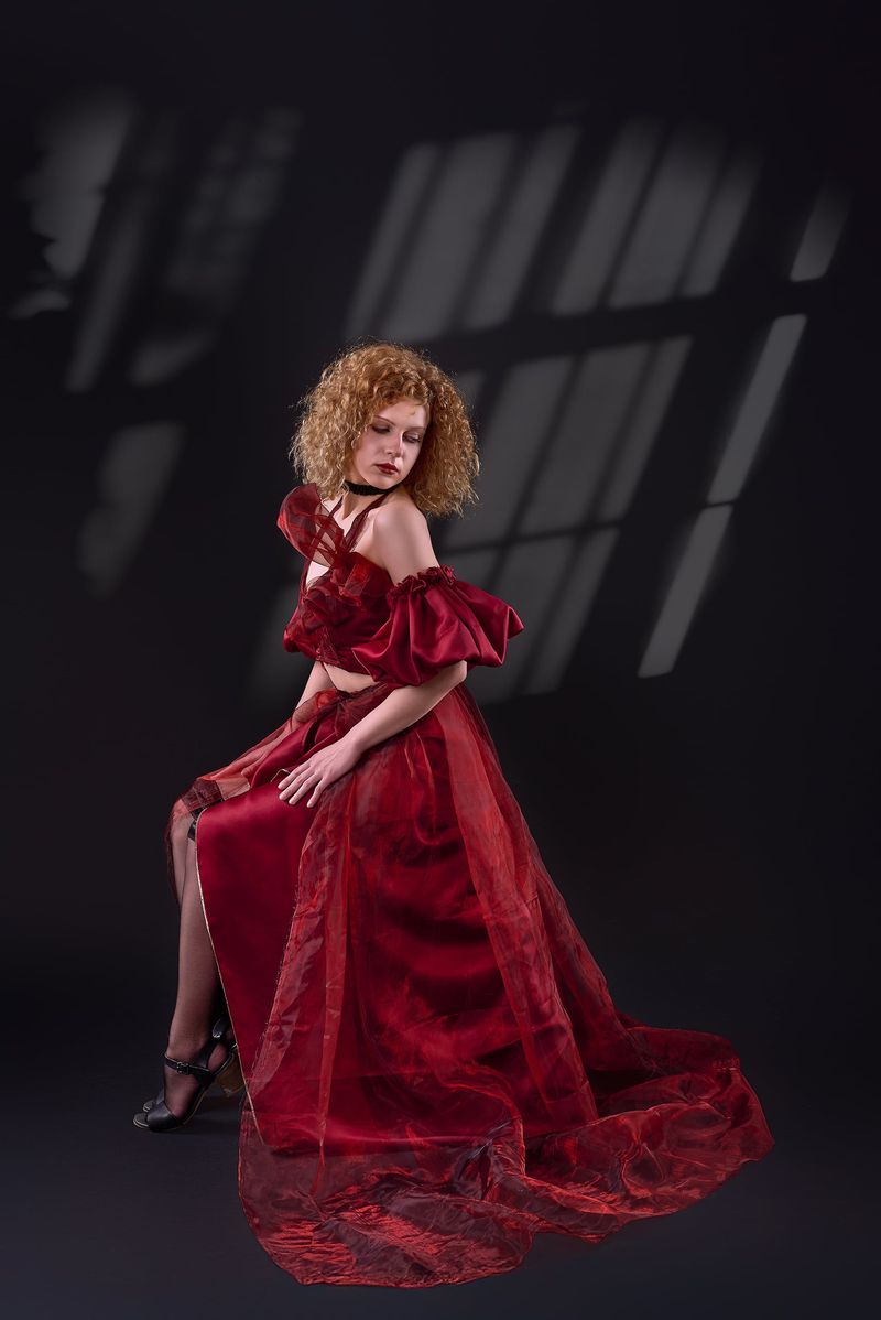 Red organza gown with a full layered skirt and puff sleeves, shown seated