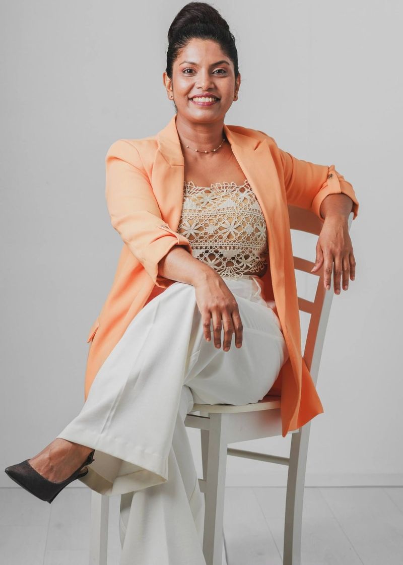 Portrait of Thenu, the designer behind Tikki ja Tyyli, seated in a peach blazer and lace top